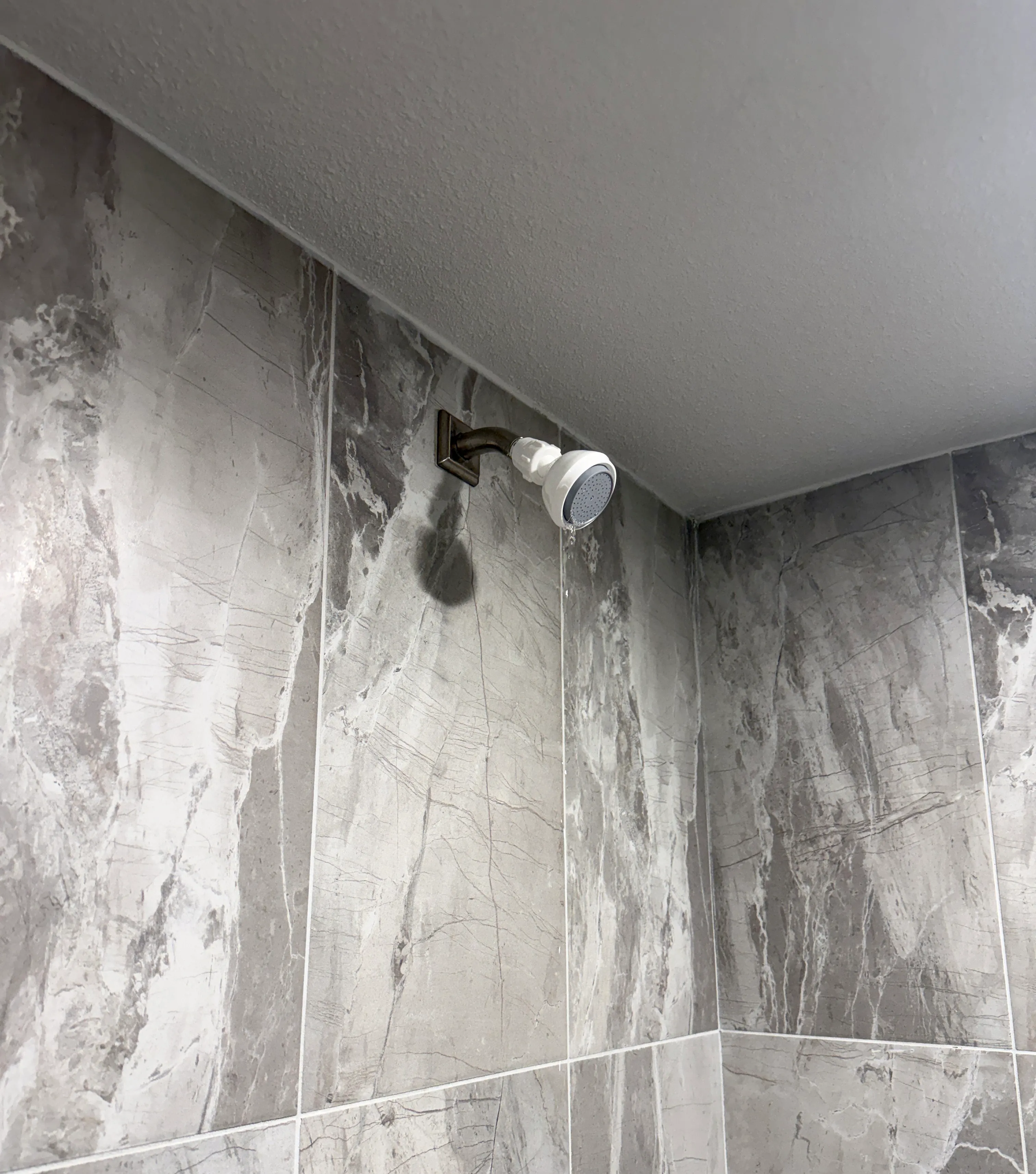 The white Siroflex Ultra installed on a shower arm against gray marble tile.
